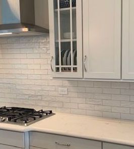 Kitchen with white cabinets, light-colored brick backsplash, and a stovetop.