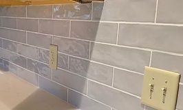 Gray subway tile backsplash with white grout, electrical outlets.