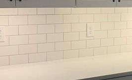 White subway tile backsplash with electrical outlets above a white countertop.