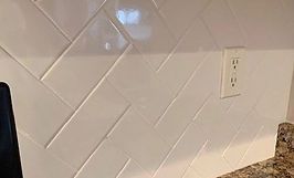 White herringbone tile backsplash with electrical outlet.