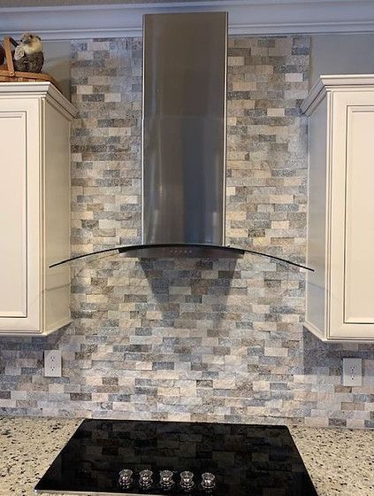 Kitchen backsplash with brick-like gray and white tiles, stainless steel range hood, and white cabinets.