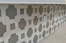 Gray and white patterned tile backsplash with a white outlet.