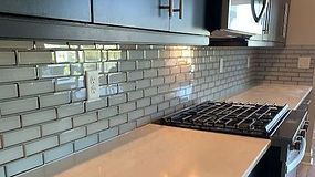 Gray subway tile backsplash in kitchen, dark cabinets, gas stovetop on a white countertop.