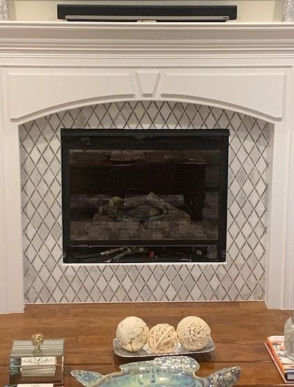 Fireplace with white mantle, diamond-patterned tile surround, and logs inside.