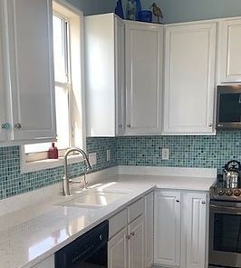 White kitchen with a blue tile backsplash, white countertops, and stainless steel appliances.