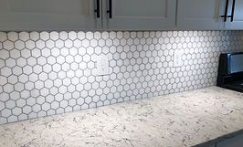 White hexagon tile backsplash above a light gray countertop, with white cabinets and black hardware.