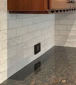 White subway tile backsplash with a dark outlet and a dark granite countertop.