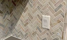 Herringbone pattern tile wall with white light switch.