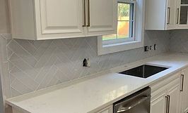 White kitchen with quartz countertops, herringbone backsplash, and stainless steel appliances.