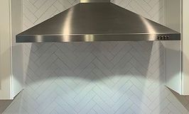 Stainless steel range hood over herringbone tile backsplash.