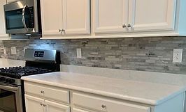 White kitchen cabinets, countertop, and backsplash with a stainless steel range and microwave.
