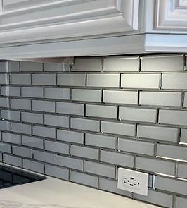 Silver subway tile backsplash under white cabinets in kitchen.