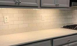 Kitchen with light-colored countertops, tiled backsplash, gray cabinets, and a stove.
