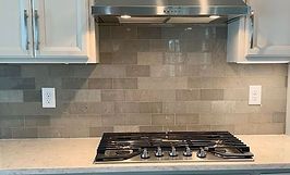 Kitchen backsplash with grey tiles, stove, and white cabinets.