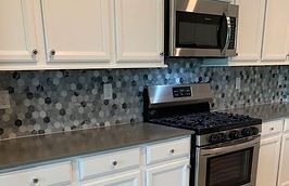 Kitchen with white cabinets, stainless steel appliances, and hexagon tile backsplash.