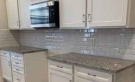 White kitchen cabinets, granite countertops, subway tile backsplash, microwave.