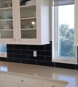 Kitchen with white cabinets, black subway tile backsplash, and a window with a view.