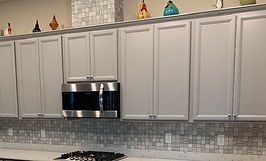 Light gray kitchen cabinets with stainless steel microwave, tiled backsplash, and decorative items.