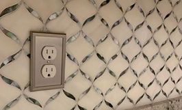 Off-white patterned tile backsplash with a silver inlay design. A light-colored electrical outlet is on the left.