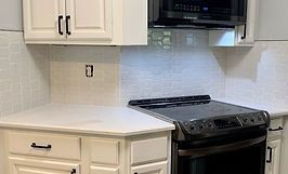 White kitchen cabinets, countertop, and appliances. Black oven and microwave. Light tile backsplash.