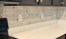 Kitchen backsplash with patterned tiles above a white countertop, with electrical outlets.