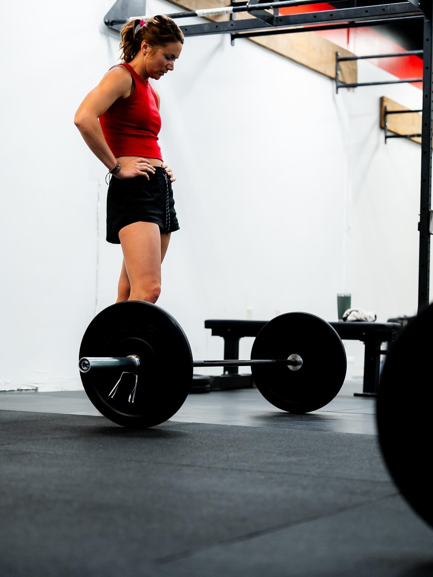 Person standing beside a barbell in a gym, looking down at the floor.