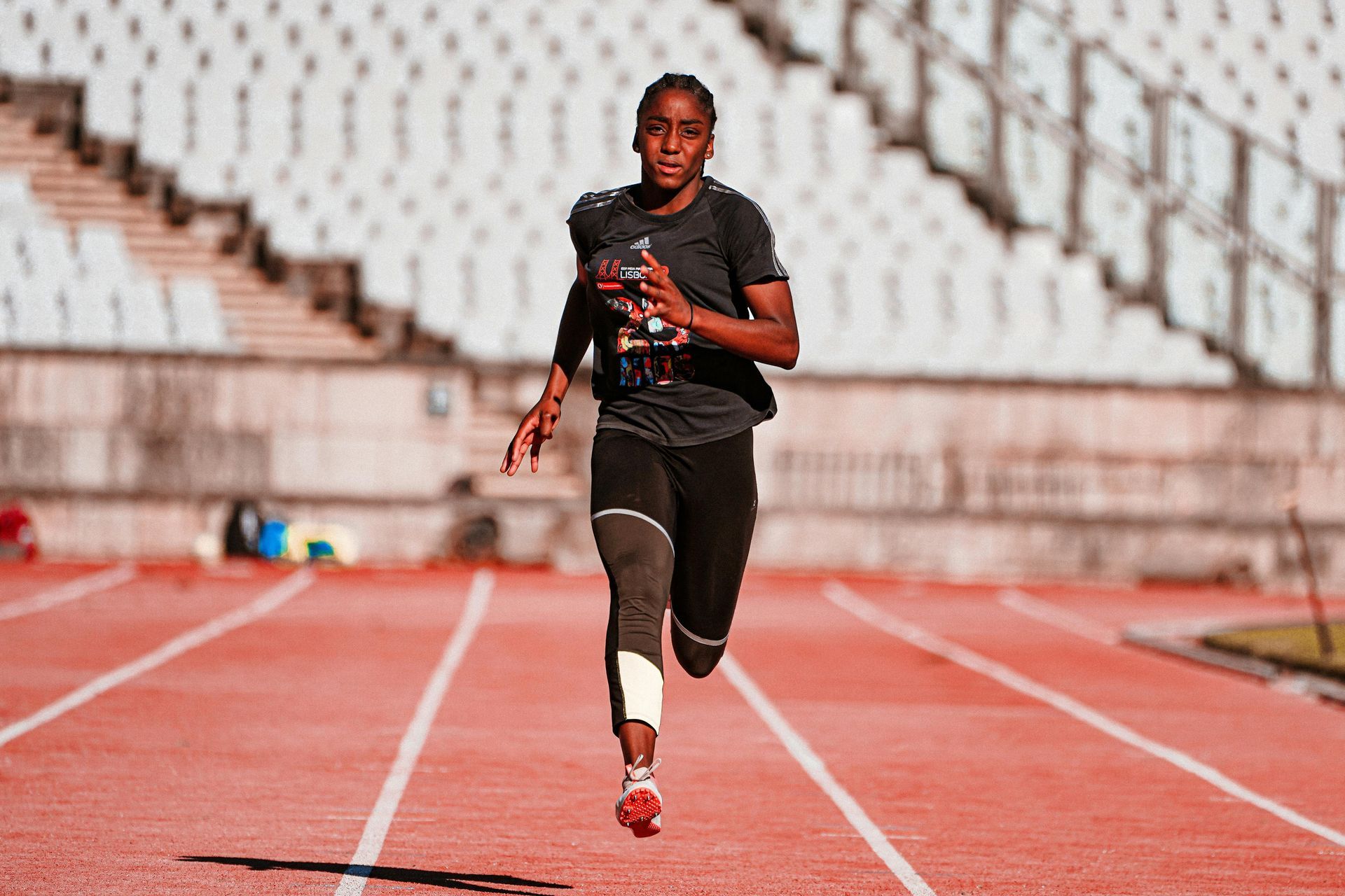 Runner sprinting on a track toward the camera, wearing black and red athletic gear.