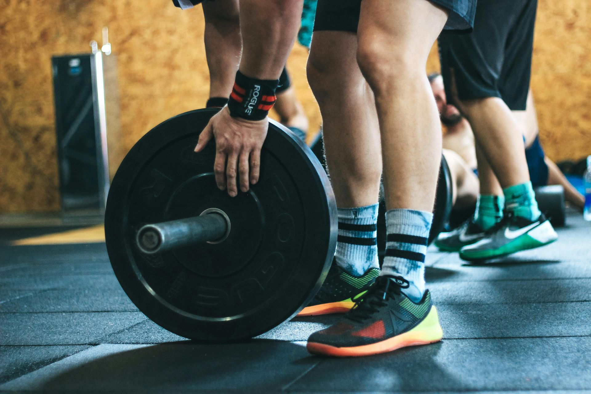People lifting a barbell in a gym, close-up of legs and hands with weight plates on the floor
