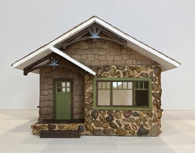 Small rustic cottage with stone base, brown shingle siding, green door, and front window