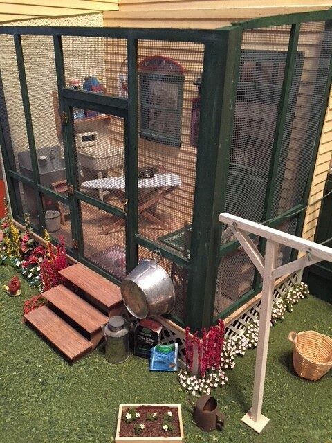 Backyard chicken coop with mesh walls, wooden steps, potted flowers, and a metal feeder beside it