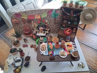 Miniature craft room display with tiny tables, shelves, potted plants, and colorful handcrafted items on the floor