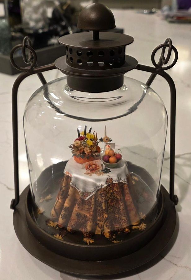 A glass cloche over a plated dessert on a dark tray, topped with flowers and fruit.