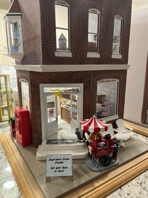 Miniature brick storefront with a red-and-white striped cart and small display signs in a glass case
