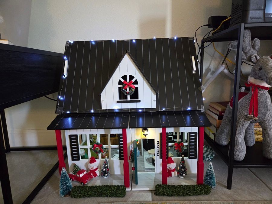 Decorated miniature house with Christmas lights, wreaths, and a lit front porch on a table