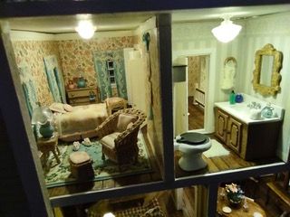 Two-room miniature dollhouse scene with a bedroom and a bathroom, shown through a window.