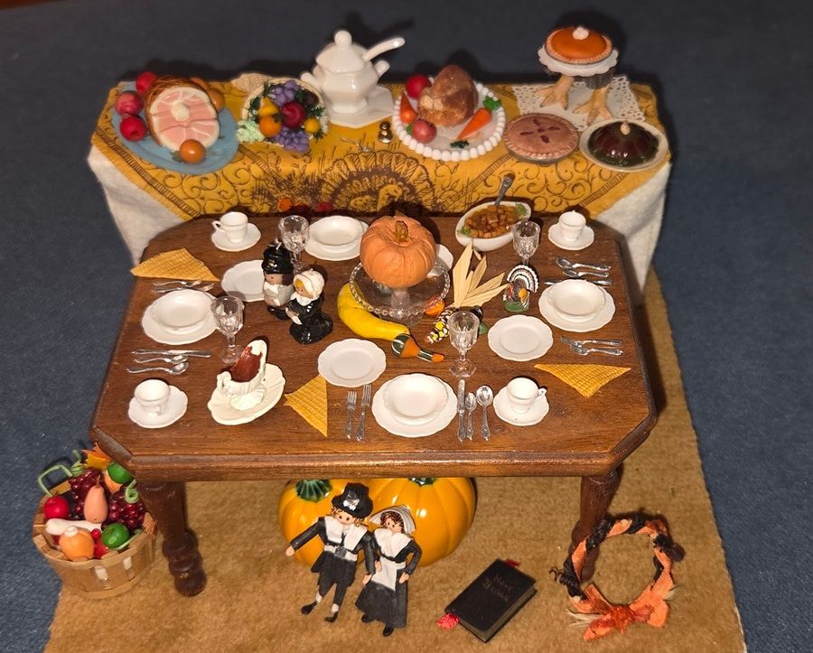 Miniature dining room table set with tea, pastries, cups, and tiny dolls in a display scene