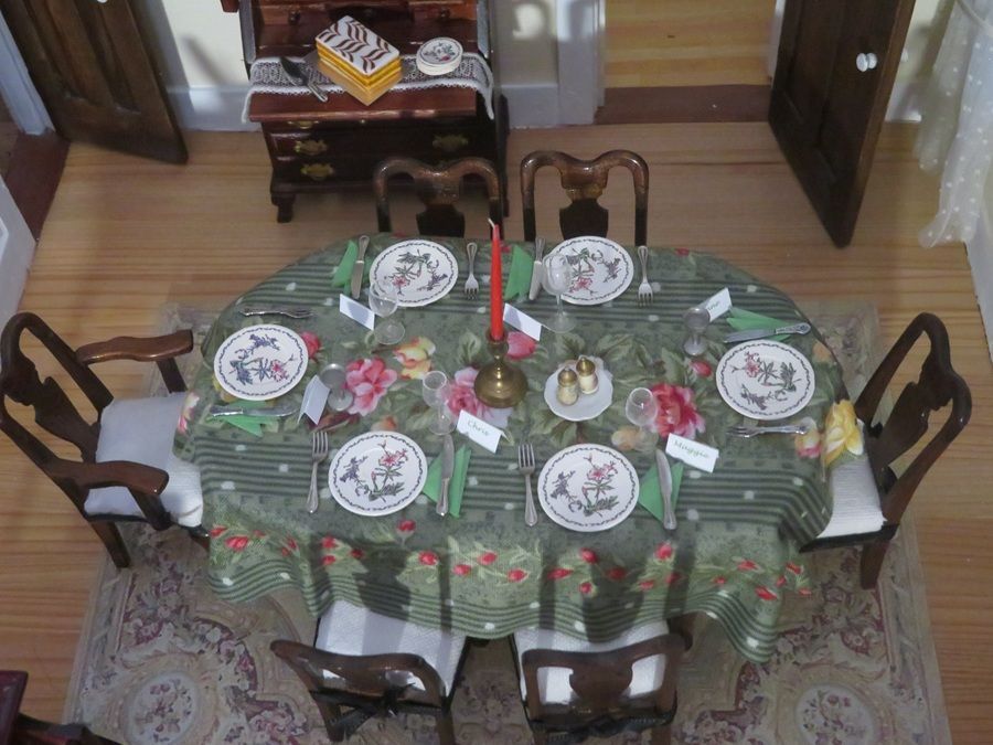 Round dining table set for a meal, with patterned green tablecloth, plates, chairs, and a candle centerpiece.