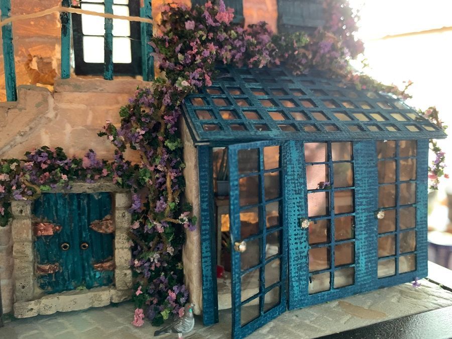 Blue garden shed with glass-paneled doors, teal shutters, and purple flowers climbing the walls.