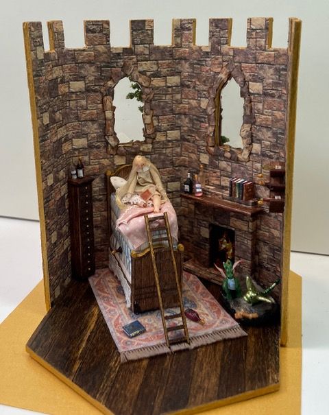 Miniature stone room diorama with a robed figure on a bed, ladder, shelves, and a wooden floor.