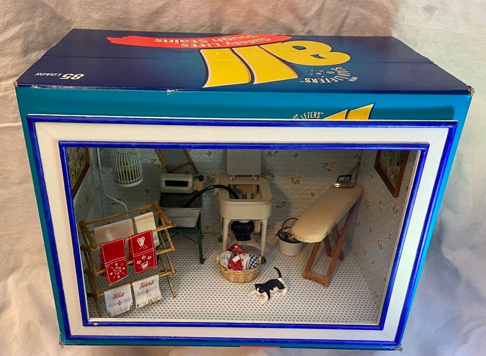 Miniature room scene in a blue display box with tiny furniture, red chairs, and a small cat figurine
