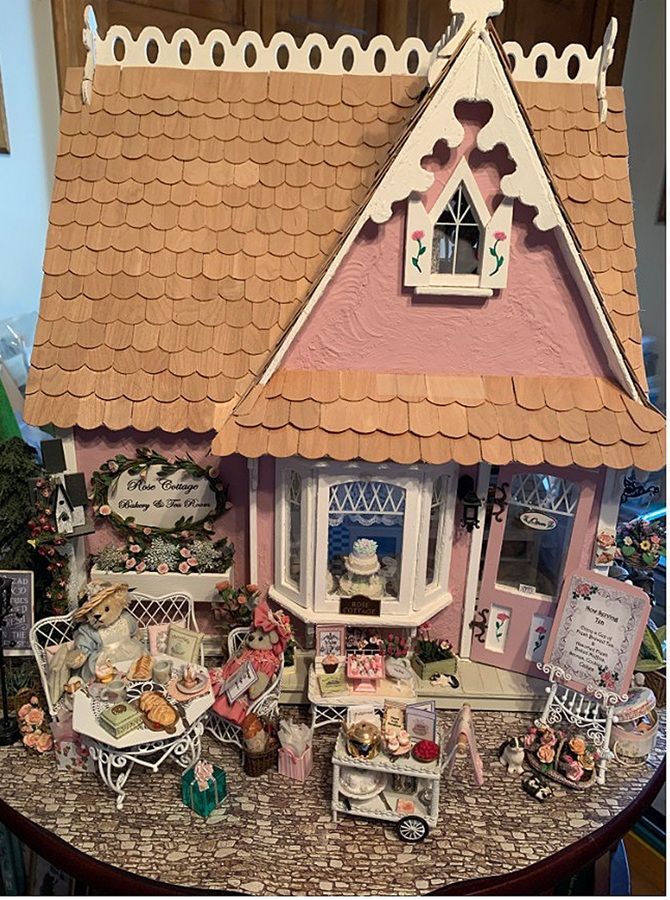 Miniature pink dollhouse with a tiled roof, decorated porch, and tiny figures and furniture in front