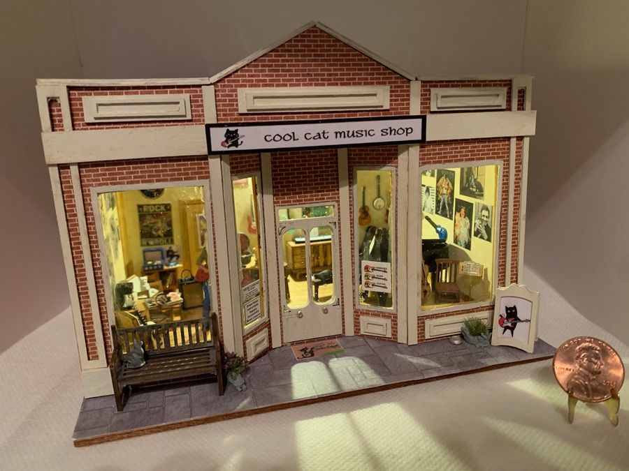Miniature storefront model of a cozy cafe with warm lights, brick facade, and a tiny bench out front.