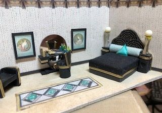 Miniature bedroom with black-and-turquoise bed, vanity, framed art, and patterned rug.