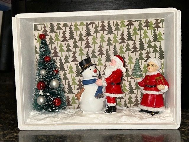 Miniature winter scene with a decorated tree, snowman, Santa, and a figure in red in a snowy box display