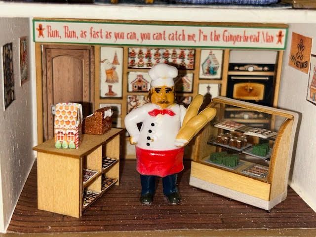 Toy bakery display with a chef figurine beside pastries, bread, and a glass display case