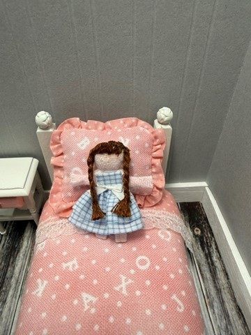 Small bed with pink star bedding and a doll sitting against pillows in a gray-walled room.