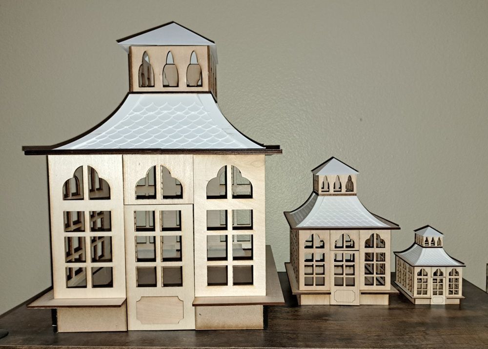 Three white decorative model houses with gray roofs arranged on a wooden table.