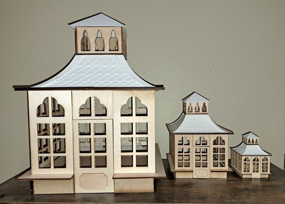 Three white decorative model houses with gray roofs arranged on a wooden table.