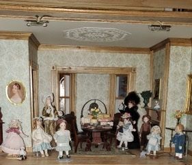 Miniature dollhouse room with Victorian-style dolls, furniture, and ornate gold trim.