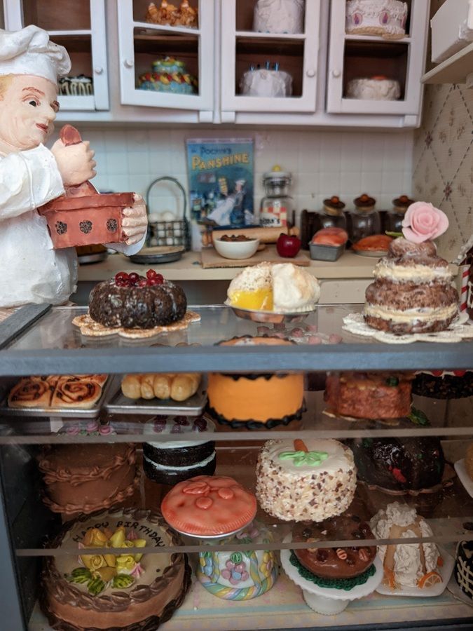 Display of assorted cakes and pastries in a bakery case with a chef figurine on the left